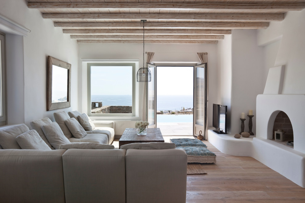 На фото: гостиная комната в морском стиле с белыми стенами, светлым паркетным полом, стандартным камином, отдельно стоящим телевизором, бежевым полом, балками на потолке и деревянным потолком