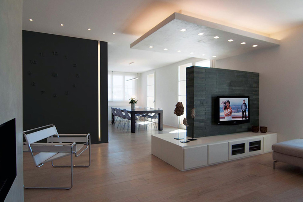 Foto de salón para visitas abierto contemporáneo grande con paredes grises, chimenea lineal, marco de chimenea de hormigón, televisor colgado en la pared y suelo de madera clara