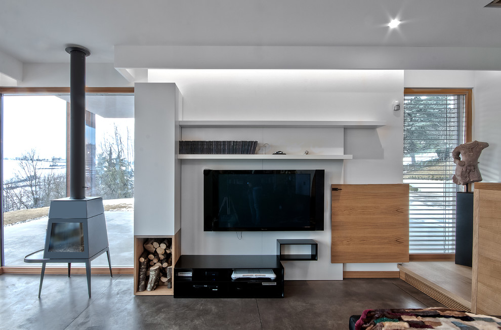 Immagine di un grande soggiorno design aperto con libreria, pareti bianche, pavimento in cemento, stufa a legna, cornice del camino in metallo e TV a parete