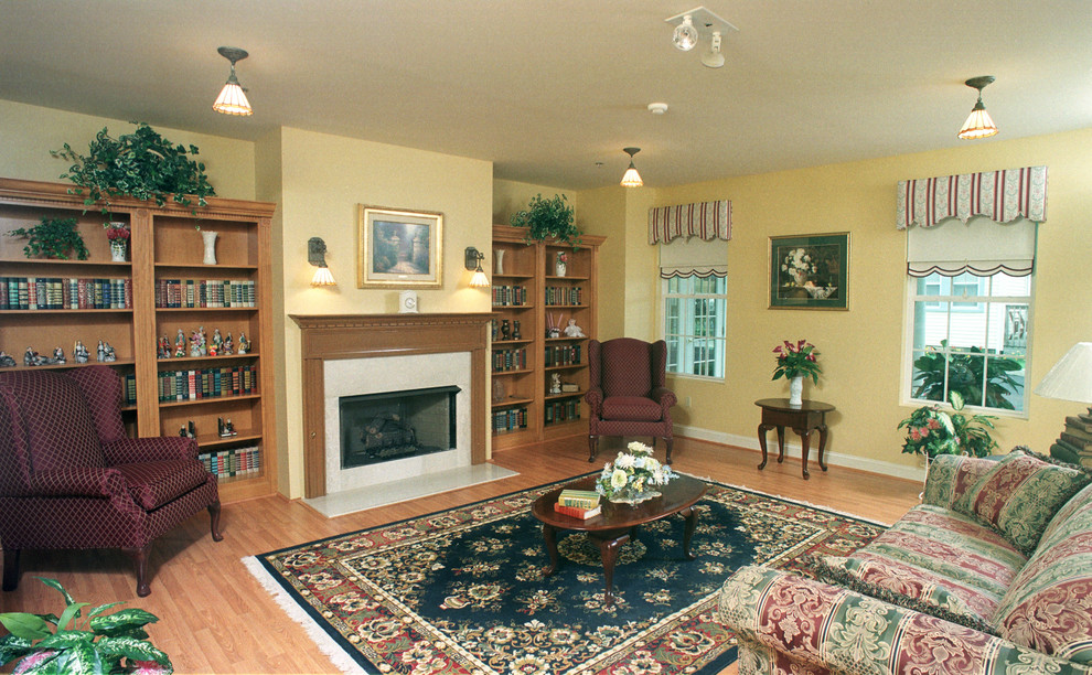 Foto på ett stort vintage separat vardagsrum, med ett bibliotek, gula väggar, ljust trägolv och en standard öppen spis