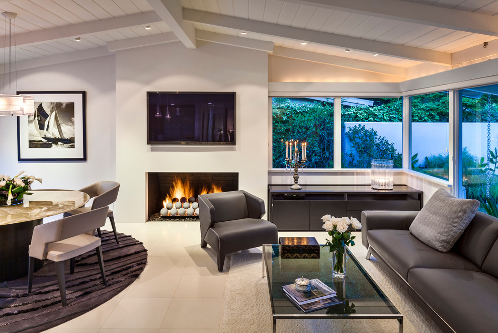 サンタバーバラにある高級な中くらいなミッドセンチュリースタイルのおしゃれなLDK (標準型暖炉、壁掛け型テレビ、白い壁、ライムストーンの床、漆喰の暖炉まわり) の写真