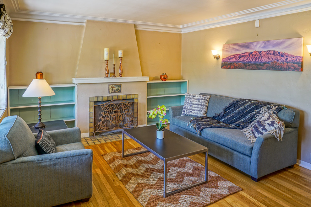 Cette photo montre un petit salon craftsman fermé avec une salle de réception, un mur beige, parquet clair, une cheminée standard et un manteau de cheminée en plâtre.