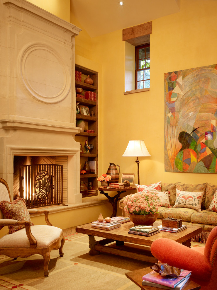 Пример оригинального дизайна: гостиная комната в средиземноморском стиле с желтыми стенами и фасадом камина из камня