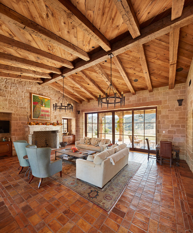 Aménagement d'un salon montagne de taille moyenne et ouvert avec tomettes au sol, une cheminée standard, un manteau de cheminée en pierre et un sol orange.