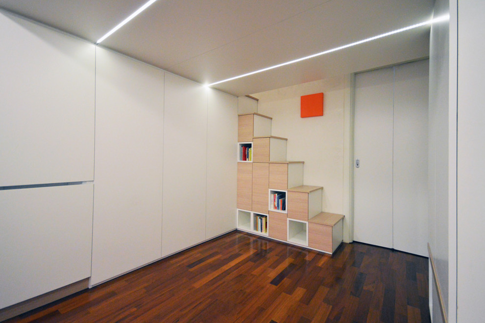 Bild på ett litet funkis allrum med öppen planlösning, med ett bibliotek, vita väggar, målat trägolv och brunt golv