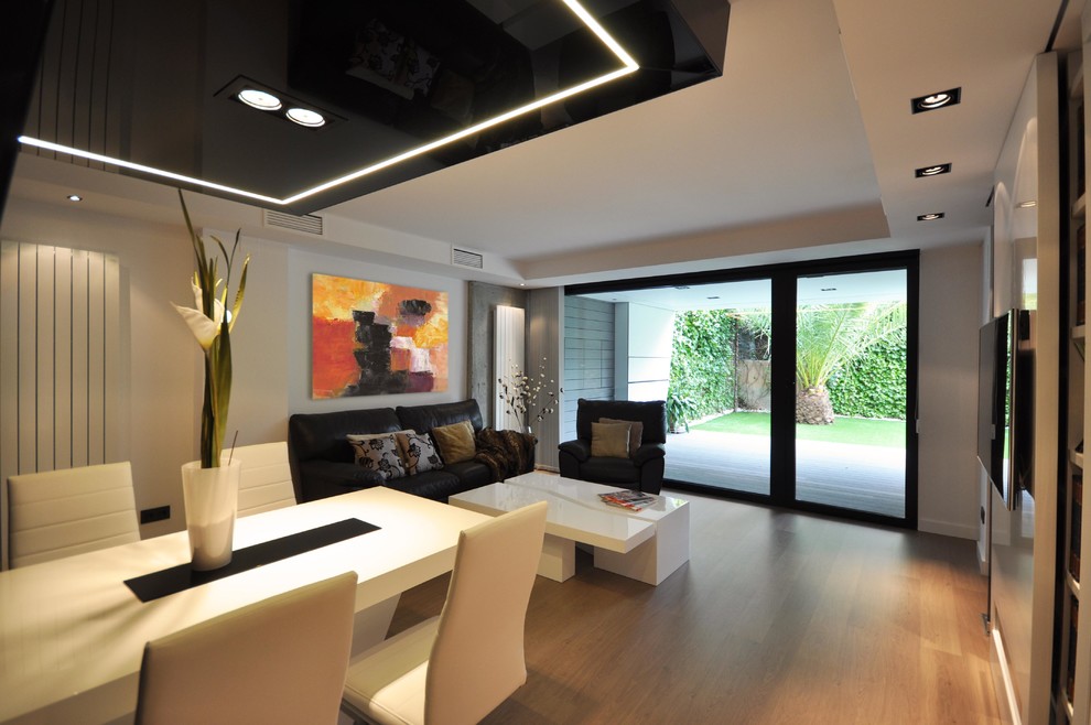 Diseño de salón abierto moderno de tamaño medio con paredes blancas, suelo de madera clara y televisor colgado en la pared