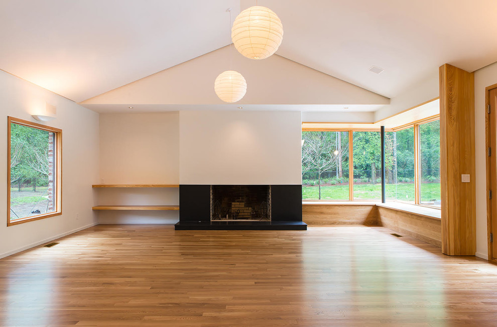 Immagine di un soggiorno minimal di medie dimensioni con sala formale, pareti bianche, pavimento in legno massello medio, camino classico e cornice del camino in pietra