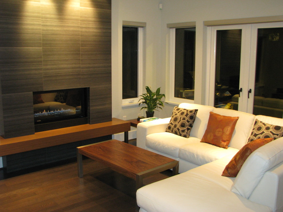 Photo of a medium sized contemporary formal enclosed living room in Vancouver with white walls, dark hardwood flooring, a standard fireplace, a wooden fireplace surround, a freestanding tv and brown floors.