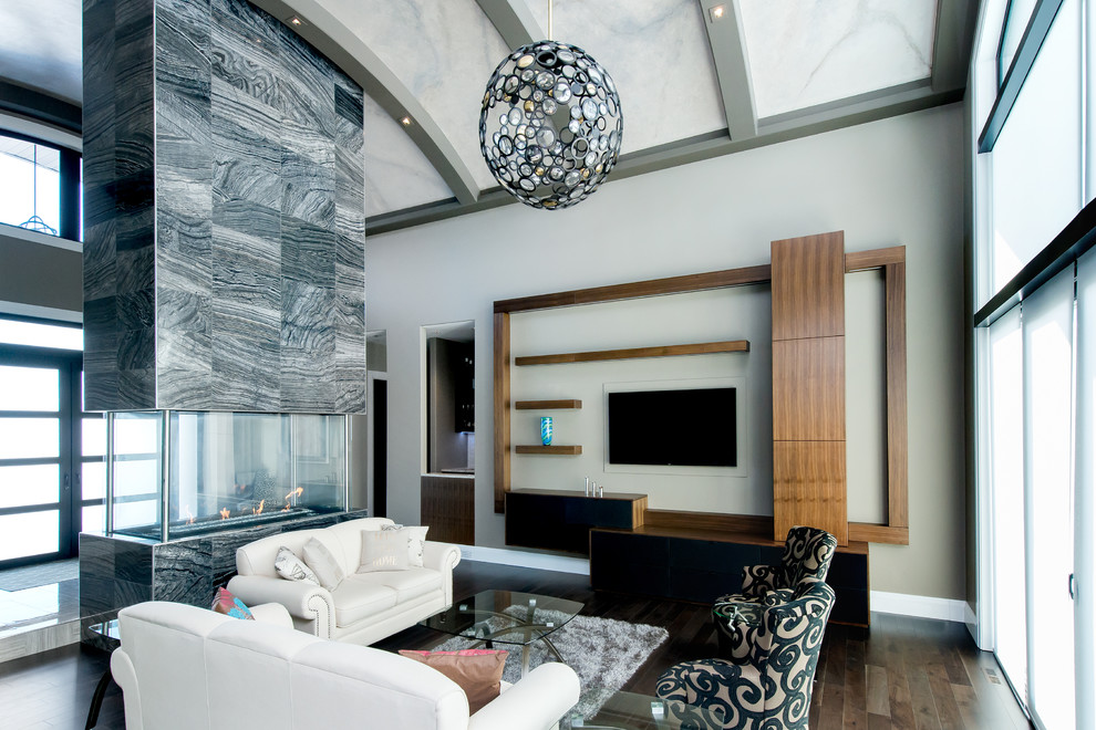 Пример оригинального дизайна: большая открытая гостиная комната в современном стиле с серыми стенами, темным паркетным полом, двусторонним камином, фасадом камина из плитки и телевизором на стене