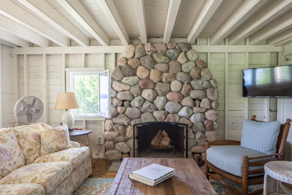 Imagen de salón cerrado de estilo de casa de campo pequeño con paredes blancas, suelo de madera en tonos medios, todas las chimeneas, marco de chimenea de piedra y televisor colgado en la pared