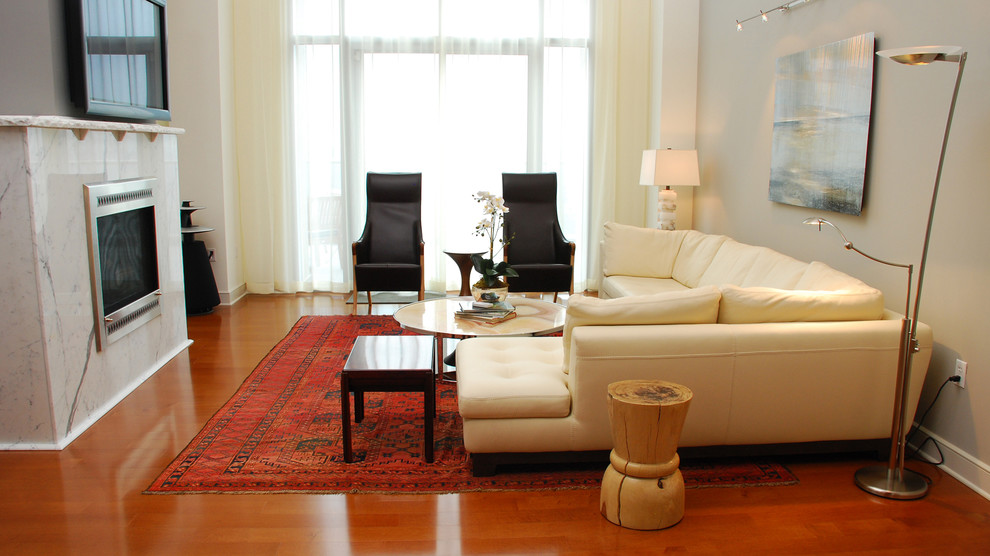 Пример оригинального дизайна: большая парадная, двухуровневая гостиная комната в современном стиле с серыми стенами, паркетным полом среднего тона, стандартным камином, фасадом камина из плитки и телевизором на стене