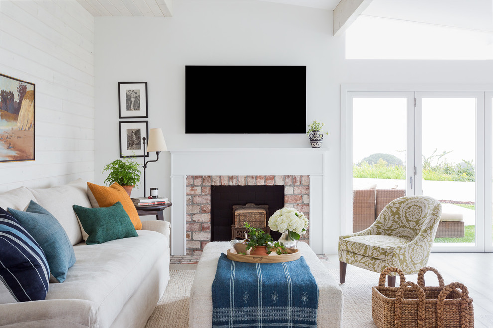 Inspiration for a medium sized beach style open plan living room in Los Angeles with white walls, light hardwood flooring, a standard fireplace, a brick fireplace surround, a wall mounted tv and beige floors.