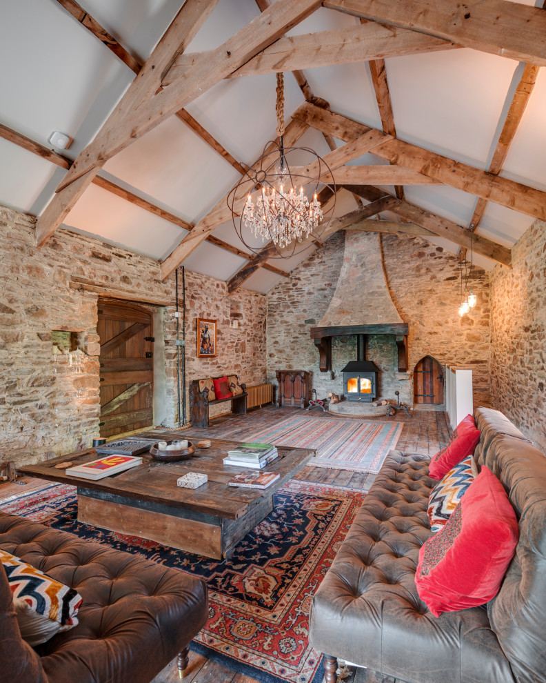 Großes, Offenes Landhaus Wohnzimmer mit brauner Wandfarbe, dunklem Holzboden, Kaminofen, braunem Boden, freigelegten Dachbalken und gewölbter Decke in Devon