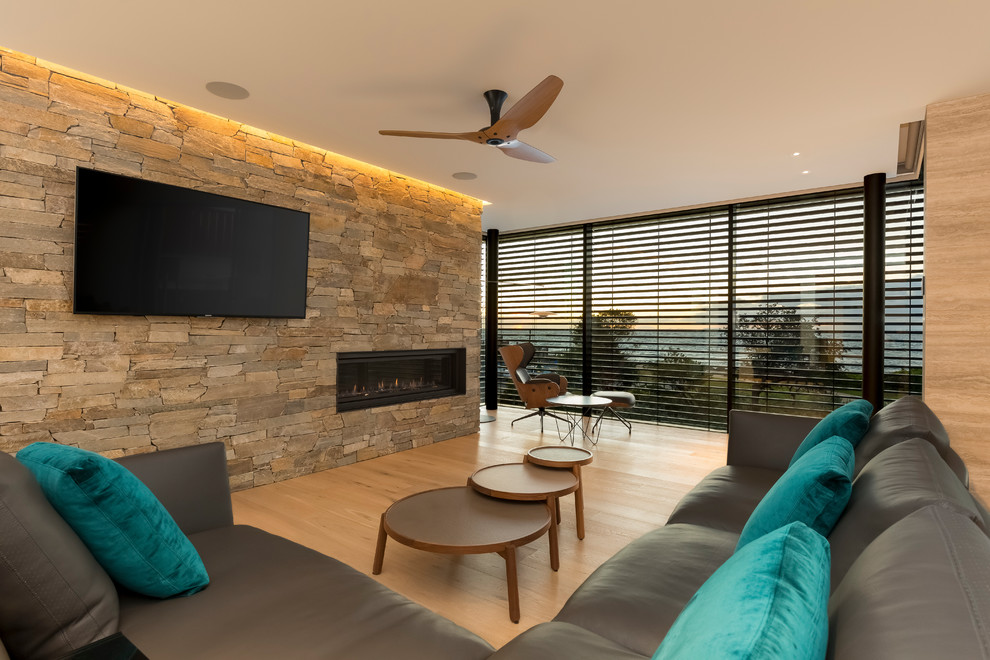 Imagen de salón abierto actual grande con paredes multicolor, suelo de madera clara, chimenea lineal, marco de chimenea de piedra y pared multimedia