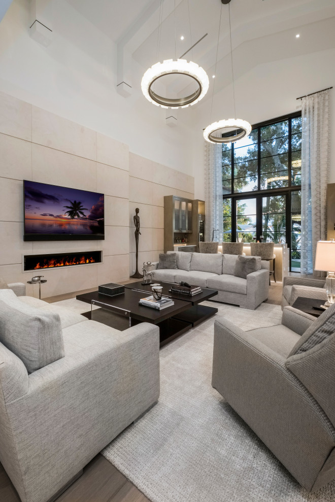 This is an example of a large traditional formal open plan living room in Miami with light hardwood flooring, a stone fireplace surround, beige walls, a ribbon fireplace, a wall mounted tv, beige floors and a vaulted ceiling.