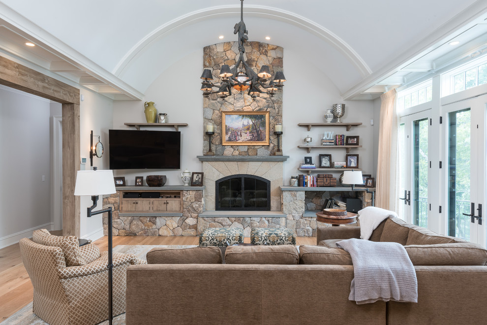 Cette image montre un grand salon rustique ouvert avec un mur blanc, parquet clair, une cheminée standard, un manteau de cheminée en pierre, un téléviseur fixé au mur et un sol beige.
