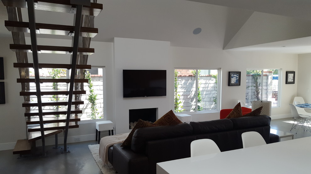 Foto de salón abierto actual de tamaño medio con paredes blancas, suelo de cemento, todas las chimeneas, marco de chimenea de yeso y televisor colgado en la pared