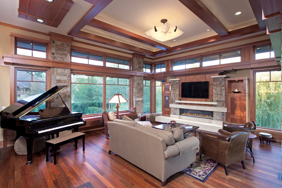Exemple d'un salon craftsman ouvert avec une salle de musique, un mur beige, un sol en bois brun, une cheminée ribbon, un manteau de cheminée en pierre et un téléviseur fixé au mur.