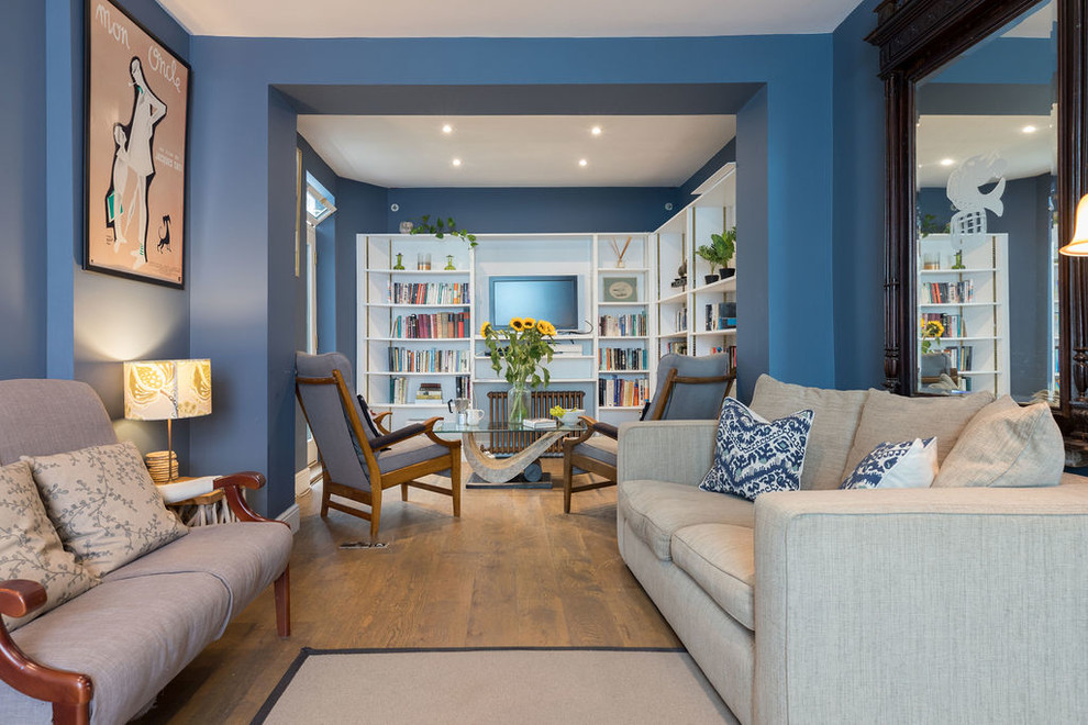 Cette photo montre un salon sud-ouest américain de taille moyenne et ouvert avec un mur bleu, un sol en bois brun, un téléviseur encastré et un sol marron.