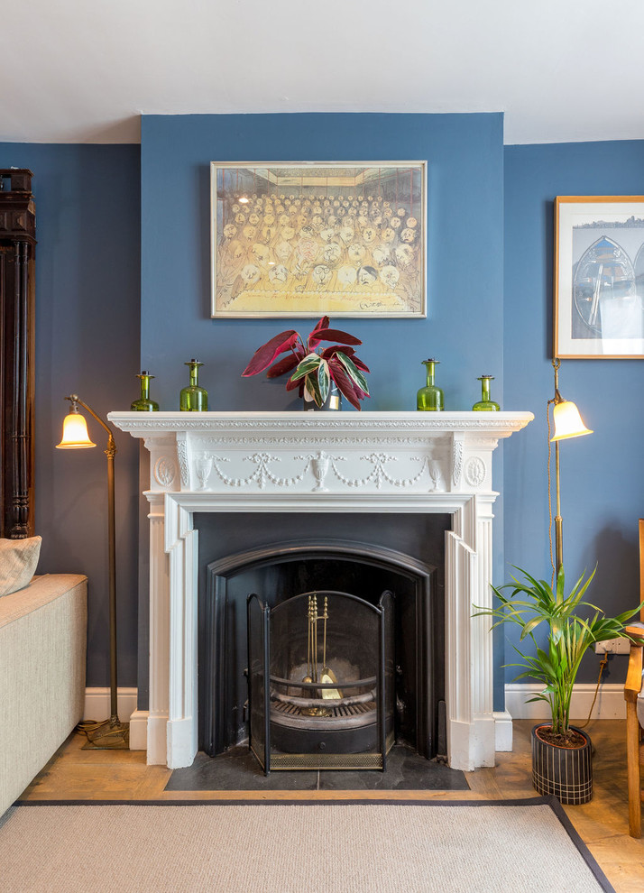 Modelo de salón abierto clásico de tamaño medio con paredes azules, suelo de madera en tonos medios, todas las chimeneas, marco de chimenea de madera y suelo marrón
