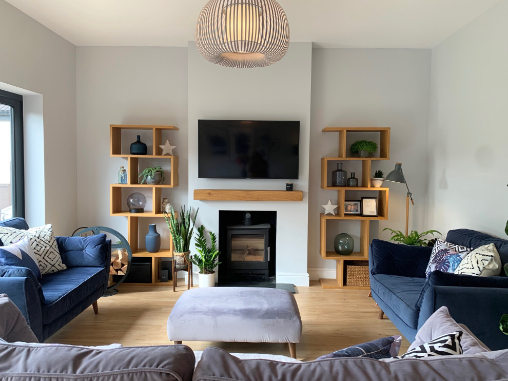 Foto di un grande soggiorno nordico aperto con libreria, pareti grigie, pavimento in laminato, stufa a legna, cornice del camino in intonaco e TV a parete
