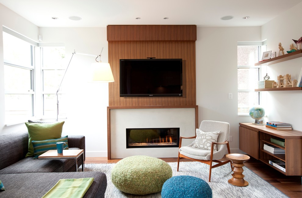 Modelo de salón para visitas actual con paredes blancas, suelo de madera en tonos medios, chimenea lineal, marco de chimenea de yeso y televisor colgado en la pared