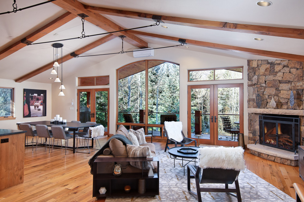 Large mountain style open concept medium tone wood floor, brown floor, vaulted ceiling and exposed beam living room photo in Denver with white walls, a corner fireplace, a stone fireplace and a tv stand