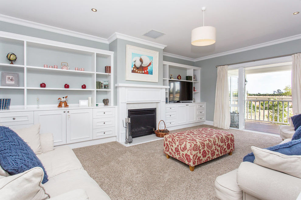 Photo of a medium sized rural formal open plan living room in Christchurch with white walls, carpet, a standard fireplace, a wooden fireplace surround, a wall mounted tv and grey floors.