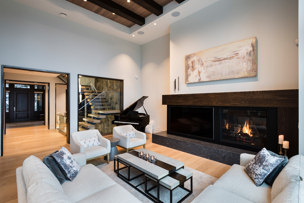 Inspiration for a large transitional open concept light wood floor and beige floor living room remodel in Vancouver with white walls, a standard fireplace, a wood fireplace surround and a media wall