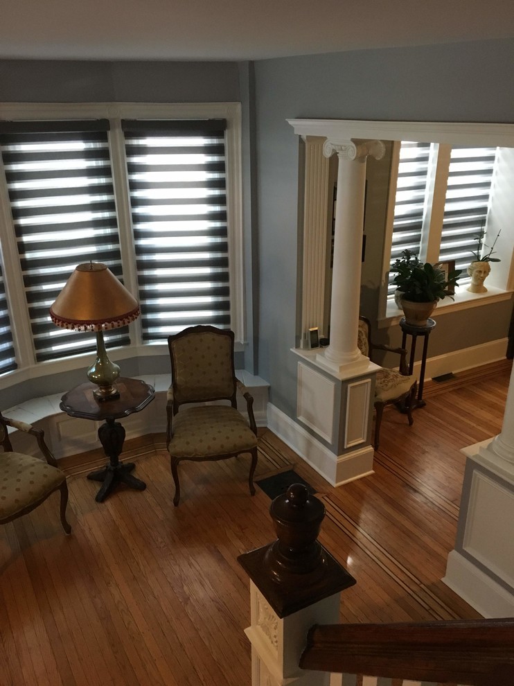 Пример оригинального дизайна: гостиная комната в классическом стиле с серыми стенами, паркетным полом среднего тона, стандартным камином, фасадом камина из дерева и коричневым полом без телевизора