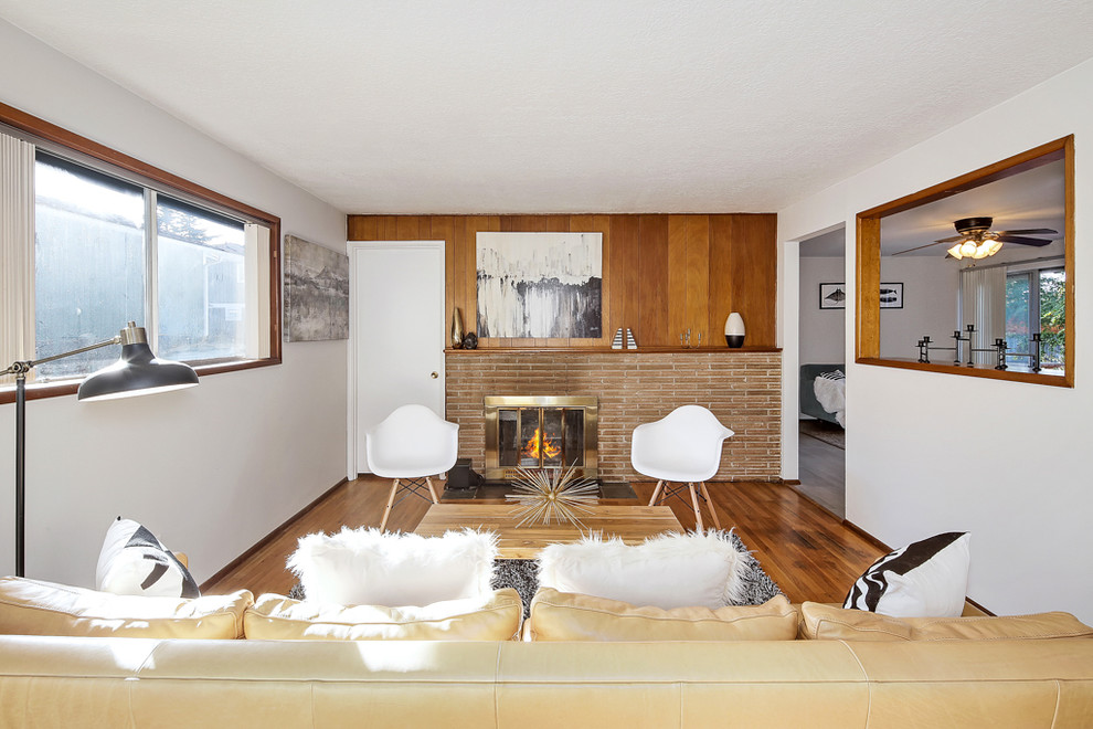 Cette image montre un petit salon vintage ouvert avec un mur gris, un sol en bois brun, une cheminée standard et un manteau de cheminée en brique.
