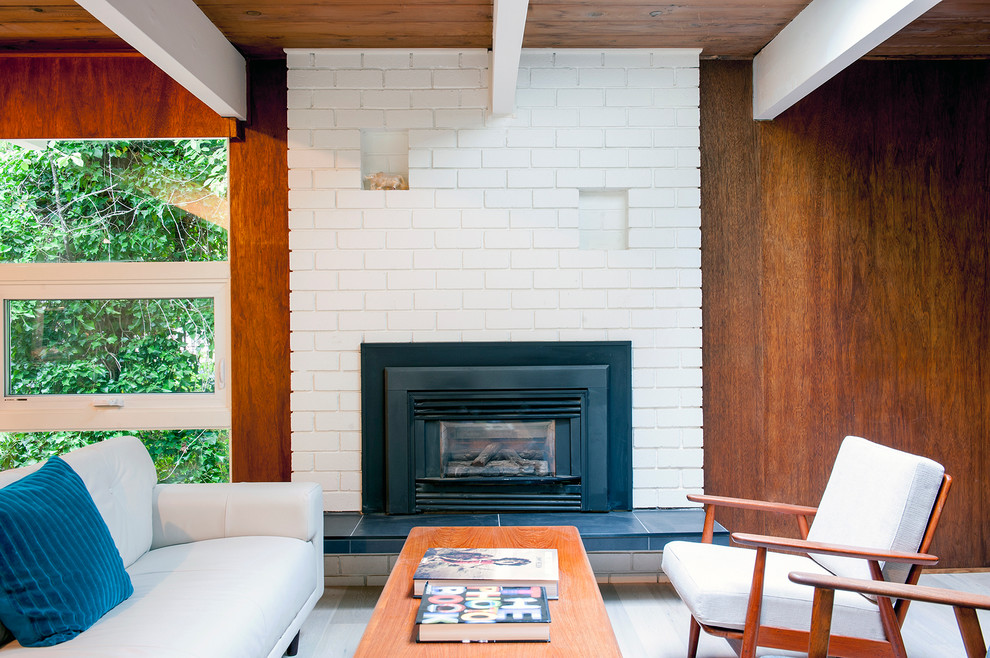 Inspiration for a mid-sized mid-century modern enclosed medium tone wood floor living room remodel in Vancouver with brown walls, a standard fireplace, a brick fireplace and a wall-mounted tv