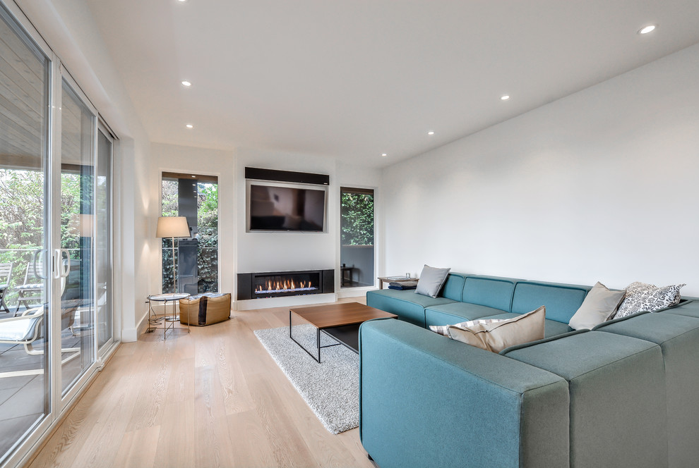 Diseño de salón abierto minimalista con paredes blancas, suelo de madera clara, chimenea lineal, marco de chimenea de yeso y televisor colgado en la pared