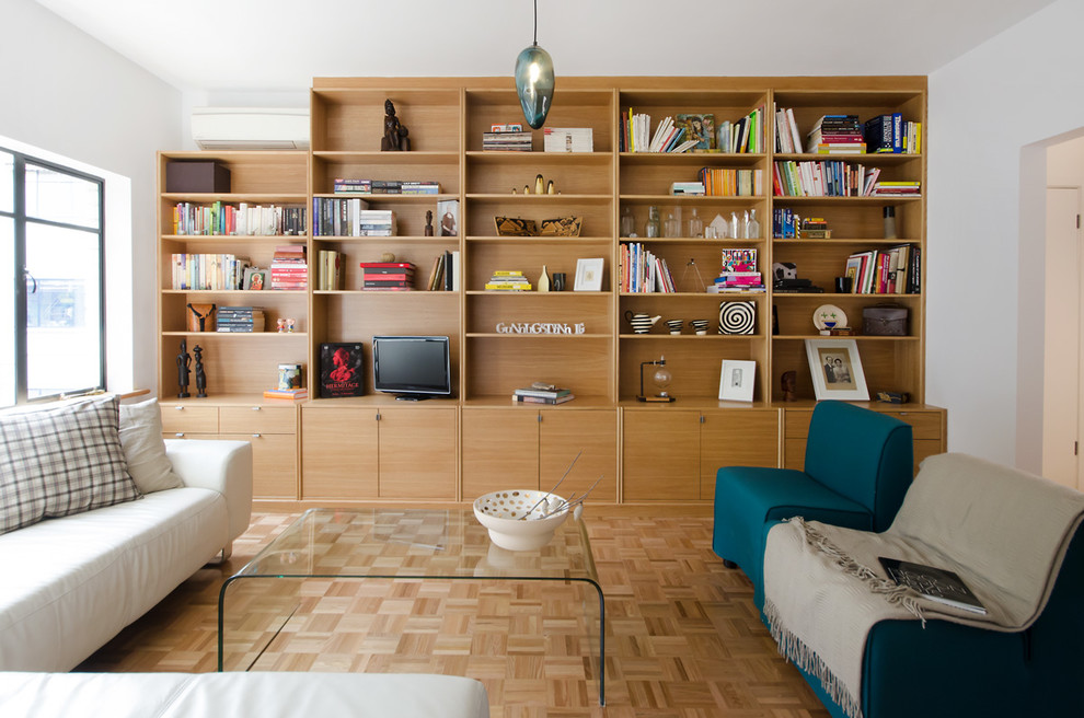 Пример оригинального дизайна: большая изолированная гостиная комната в современном стиле с с книжными шкафами и полками, белыми стенами, светлым паркетным полом и отдельно стоящим телевизором без камина