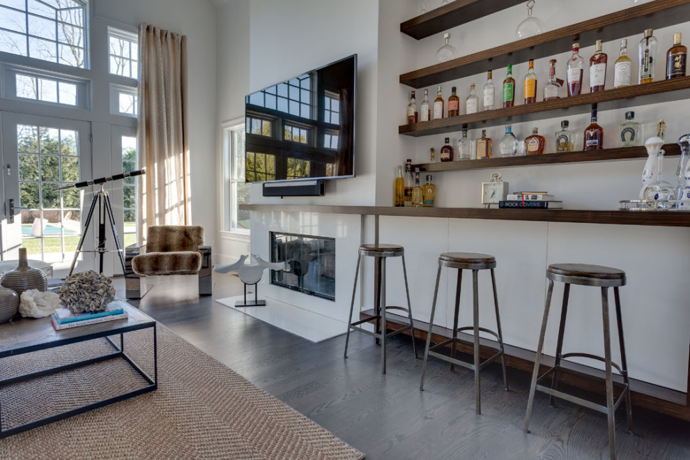 Imagen de salón con barra de bar abierto moderno con paredes blancas, suelo de madera en tonos medios, todas las chimeneas, marco de chimenea de yeso y televisor colgado en la pared