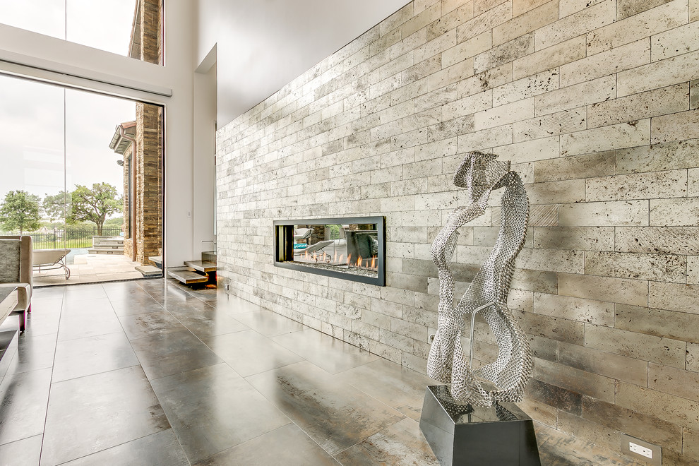 Diseño de salón abierto minimalista grande con chimenea de doble cara, marco de chimenea de piedra y televisor colgado en la pared
