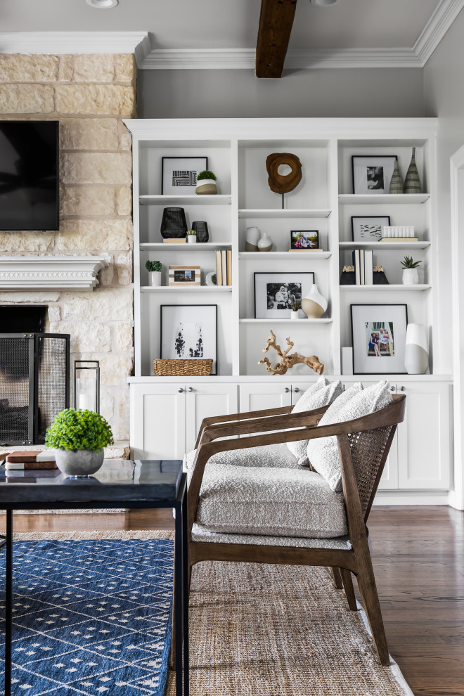 Inspiration for a traditional enclosed living room in Austin with grey walls, medium hardwood flooring, a standard fireplace, a stone fireplace surround, a wall mounted tv, brown floors and exposed beams.
