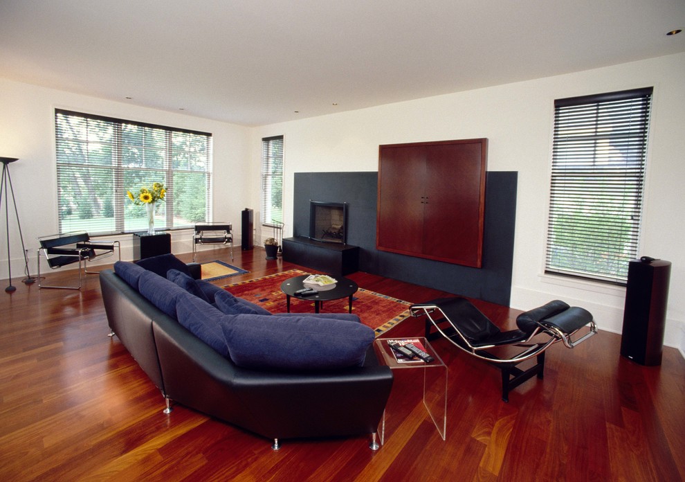 Пример оригинального дизайна: большая открытая, парадная гостиная комната в стиле модернизм с белыми стенами, темным паркетным полом, стандартным камином, фасадом камина из камня, скрытым телевизором и коричневым полом