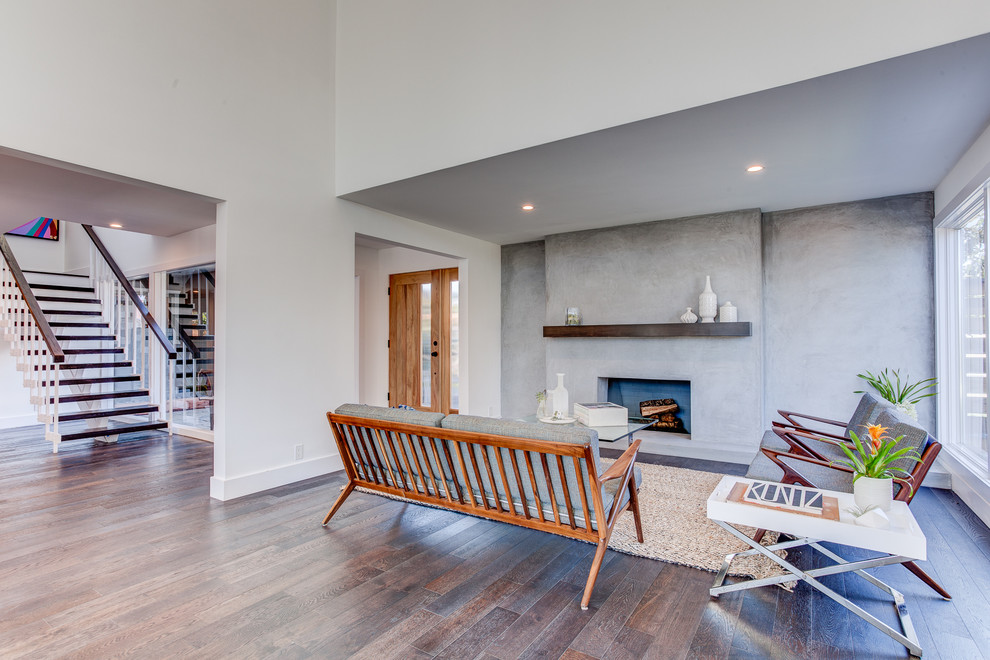Example of a mid-sized trendy formal and open concept medium tone wood floor living room design in Los Angeles with white walls, a standard fireplace, a concrete fireplace and no tv