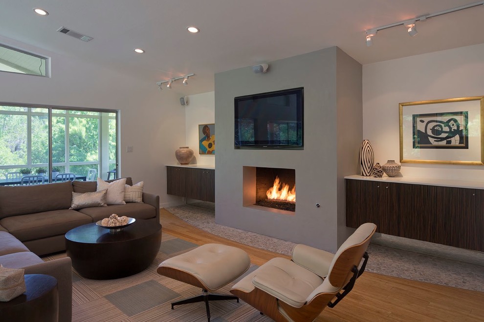 Стильный дизайн: гостиная комната в стиле ретро с серыми стенами, полом из бамбука, стандартным камином, фасадом камина из штукатурки и телевизором на стене - последний тренд
