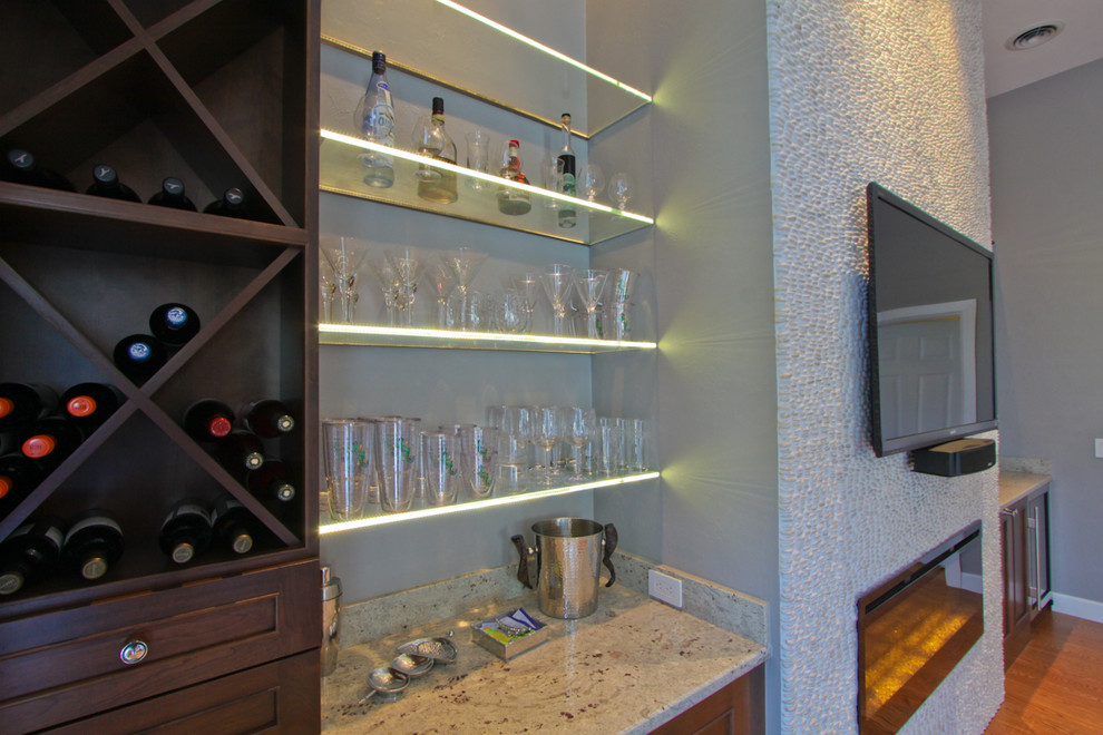 На фото: открытая гостиная комната в стиле неоклассика (современная классика) с домашним баром, серыми стенами, паркетным полом среднего тона, горизонтальным камином, телевизором на стене, фасадом камина из плитки и коричневым полом
