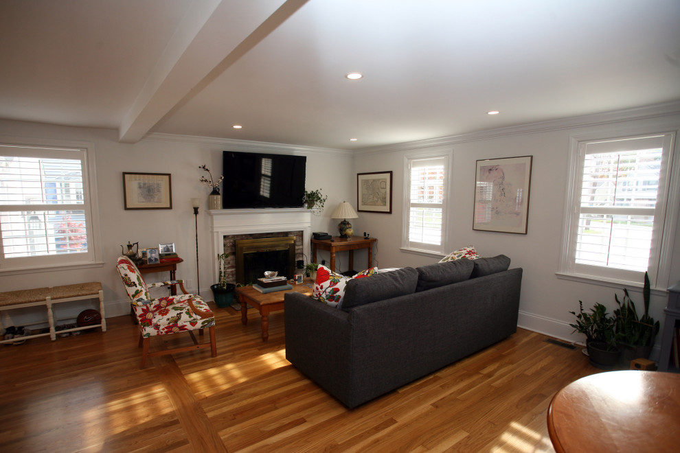 Offenes Klassisches Wohnzimmer mit grauer Wandfarbe, hellem Holzboden, Kamin, Kaminumrandung aus Holz, TV-Wand und rotem Boden in Boston