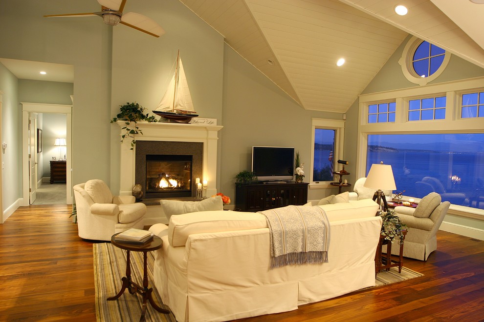 広いビーチスタイルのおしゃれなリビング (青い壁、無垢フローリング、標準型暖炉、漆喰の暖炉まわり、据え置き型テレビ) の写真