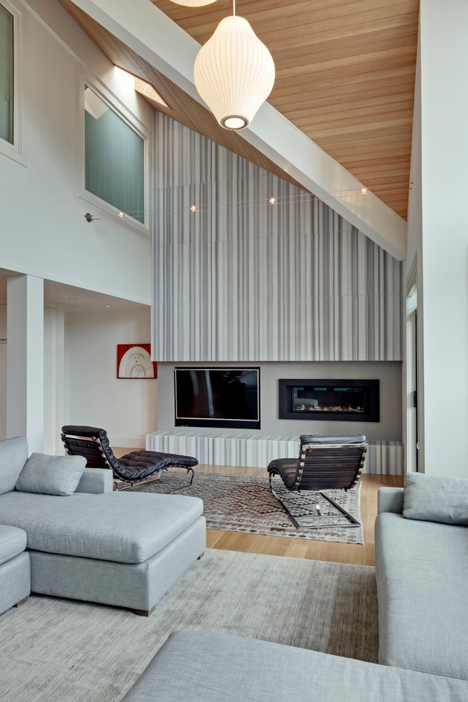 Foto de salón abierto actual grande con paredes grises, suelo de madera clara, todas las chimeneas, televisor colgado en la pared y piedra