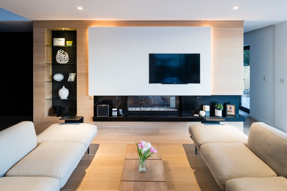 На фото: открытая гостиная комната в стиле модернизм с белыми стенами, светлым паркетным полом, стандартным камином и телевизором на стене