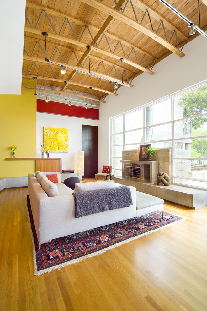 Example of a trendy open concept medium tone wood floor and orange floor living room design in Dallas with yellow walls, no tv, a standard fireplace and a concrete fireplace