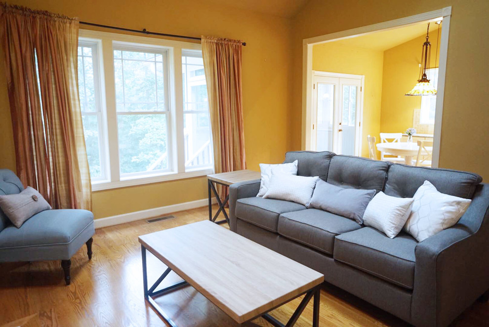 Mittelgroßes, Offenes Klassisches Wohnzimmer mit gelber Wandfarbe, hellem Holzboden, Kamin und Kaminumrandung aus Holz in Raleigh