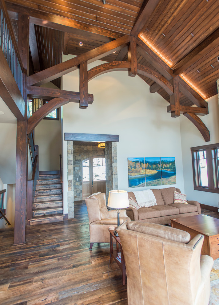 This is an example of a large rustic mezzanine living room in Boise with beige walls, dark hardwood flooring, a standard fireplace, a stone fireplace surround and brown floors.