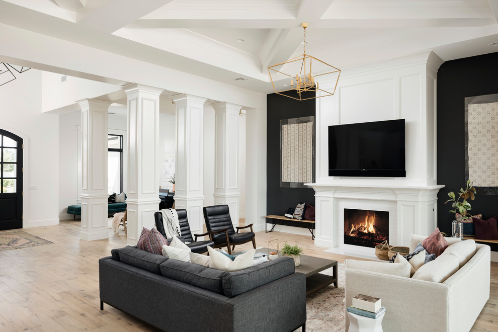 フェニックスにある高級な広いトランジショナルスタイルのおしゃれなLDK (黒い壁、淡色無垢フローリング、標準型暖炉、壁掛け型テレビ、木材の暖炉まわり、ベージュの床、黒いソファ) の写真