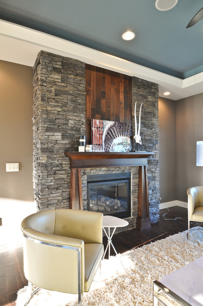 Abgetrenntes Rustikales Wohnzimmer mit grauer Wandfarbe, dunklem Holzboden, Kamin und Kaminumrandung aus Stein in Cedar Rapids
